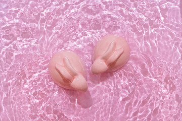 Happy Easter minimal concept. Two bunny rabbits in water on pastel pink background
