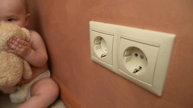 A young mother carefully plugs power outlets with special plugs to protect the baby from possible electric shock