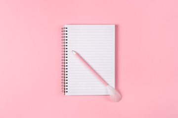 Notepad and pink pen decorated with feather on pink background. Woman power concept.