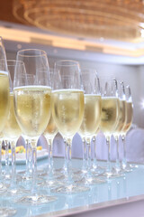 Glasses with champagne on the table. Holidays concept. Party in a large bright hall. Secular reception. Buffet at a secular party. Lots of wine glasses.Gala dinner or event. Vertical photo.
