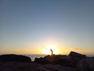 silhouette of a fisherman on the rocks and the sea