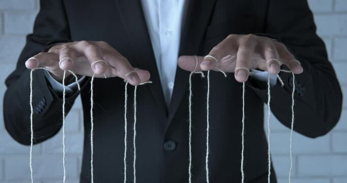 Business manipulation. A businessman man with tied fingers on a string manipulate with employees in the office.