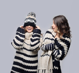 Two  girl wearing knit hat, scarf, sweater and gloves posing against   blue  background.