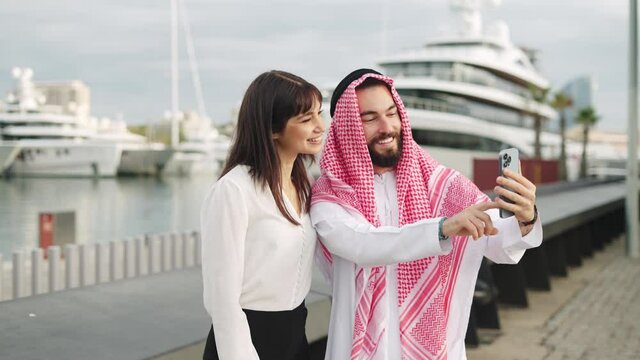 Two smiling multiracial business partners arab man and european woman taking selfie in port