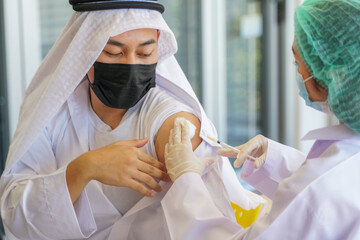 Portrait of Arab Muslim man looking at while getting covid vaccine in clinic or hospital, with hand...