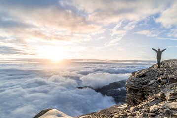 Silhouette of a man celebrating success over a sea of cloud on a mountain top in the alps during...