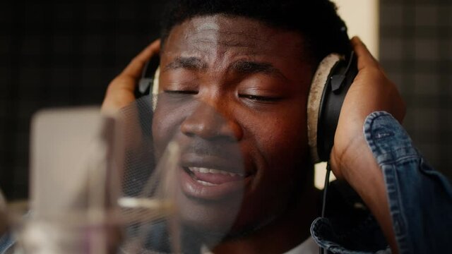 African American Male Singer Wearing Headphones Singing To Microphone In Music Studio