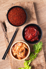 Korean kimchi cabbage with gochujang (red chili paste) and chili powder in bowl on wooden background, Table top view