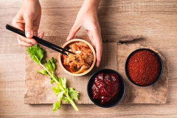 Korean kimchi cabbage eating by use chopsticks with gochujang (red chili paste) and chili powder in bowl on wooden background, Table top view - obrazy, fototapety, plakaty