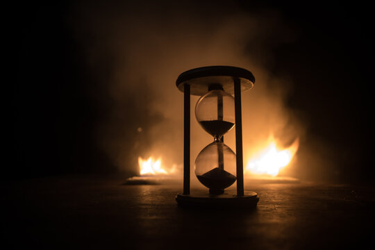 Time concept. Silhouette of Hourglass clock and old vintage wood clock with arrow and smoke on dark background with hot yellow orange red blue cold back lighting, or symbols of time with copy space