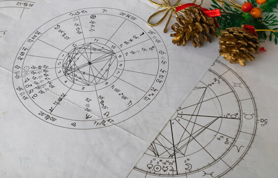 Printed astrological natal charts with Christmas pine cone decoration in the background