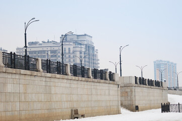 Houses on the embankment of the Amur River during a snowfall. Winter morning. Granite walls. Snow...