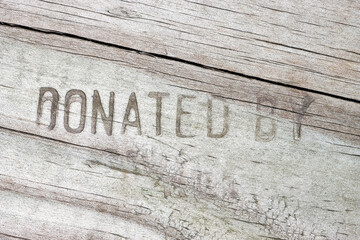 Carved Donated by text on wooden table plank