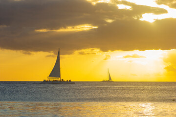 SUNSET ON THE BEACH WITH BOATS IN THE ORIZON AND ORANGE SUNLIGHT, WITH BLUE SKY AND SOME CLOUDS