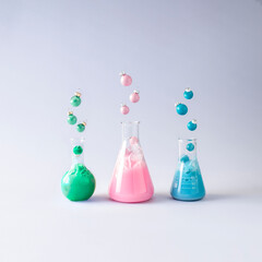 Pink, blue and green laboratory bottles with christmas baubles coming out of them. Chemical...
