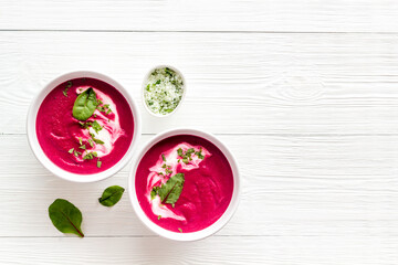 Two white bowls of red beet soup with sour cream and green herbal salt