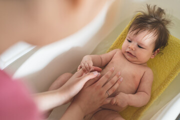 Small caucasian baby taking a bath at home - unknown woman mother holding her small child baby in plastic bath tub in room at home parenting and hygiene concept real people