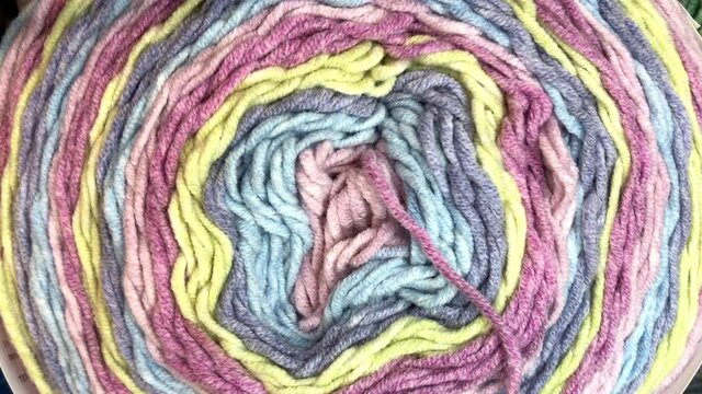 4K HD video zooming in on center of a skein of multi-colored pastel yarn with end sticking out of the center.
