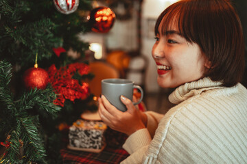 Happy women holds a cup of coffee and smell aromatic near a Christmas tree decoration