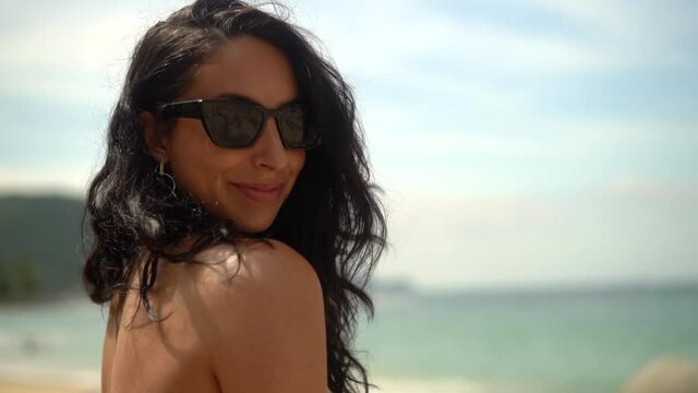 Beautiful, happy woman on the beach wearing sunglasses and smiling for the camera - close up isolated