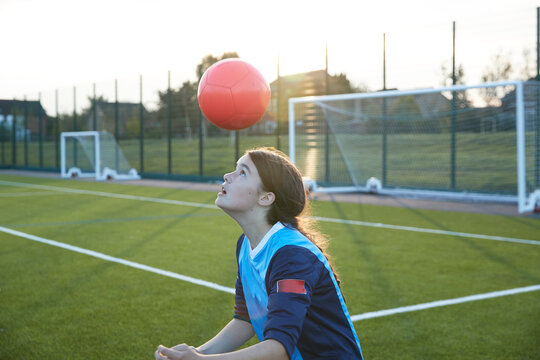 UK, Female soccer player (10-11) bouncing ball in field at sunset