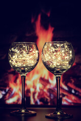 Two transparent wine glasses filled with small, shining garland lights. Beautiful, transparent glasses shine, Merry Christmas and Happy New Year.