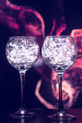 Transparent wine glasses, with shining lights of bright bulbs and a beautiful background. Shining glasses with bright lights create a festive atmosphere and a desire to celebrate Christmas and New Yea