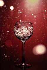 Transparent wine glass, with shining lights of bright bulbs and a beautiful background. A shining glass with bright lights creates an atmosphere of holidays and a desire to celebrate Christmas and New
