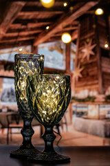 Two curly, beautiful glasses of different heights shine with light and attract attention to create a festive atmosphere. Beautiful, transparent glasses shine, Merry Christmas and Happy New Year.