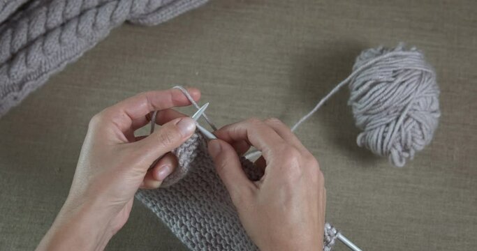 Hold needles and knitting. A woman pas her holiday with needles and woolen threads on the sofa.