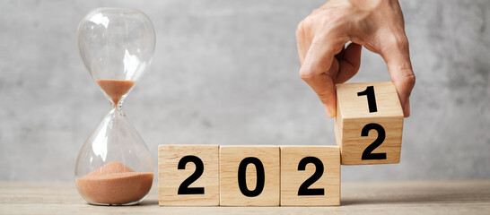 hand flipping block 2021 to 2022 text with hourglass on table. Resolution, time, plan, goal,...