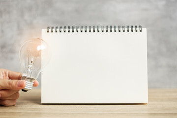 Hand holding lightbulb over blank notebook on table. New Ideas, Creative, Innovation, Imagination, inspiration, Resolution, Strategy and goal concept