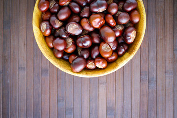 Obraz premium Chestnuts in a wooden bowl on wooden backgound