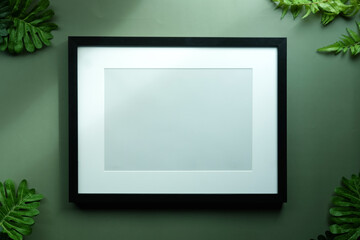 Black photo frame and green leafs on green background.