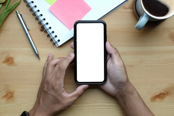 Young man holding smart phone with blank screen on wooden table.
