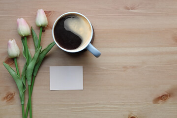 Coffee cup, sticky note and pink tulips on wooden table.