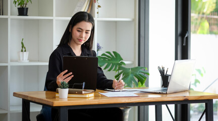 Attractive young woman entrepreneur holding digital tablet and working with laptop computer.