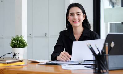 Asian businesswoman sitting at her office desk and smiling to camera.