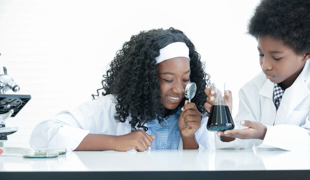 Little African kids learning chemistry and doing chemical science experiment in laboratory at school. Excited dark skinned boy and girl using magnifying glass to look at liquid in test bottle