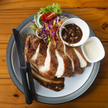 Chicken staek serve on white dish with sauceand salad.