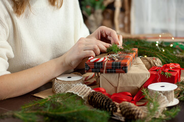 Women's hands decorate the box with the Christmas gift. Table with decor and materials for decoration. The process is needlework. Side view Selective focus