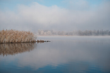 Autumn morning landscape. Sunrise over the lake in fog. The beginning of winter, the roe on the trees and grass.