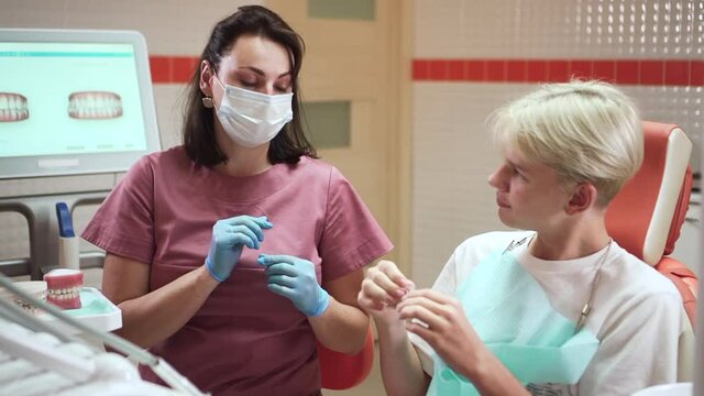 Orthodontist with teen boy and aligners. spbd Female dentist with surgical mask and teenager patient looking at new braces in contemporary hospital office