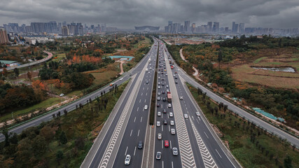 Aerial drone view of Chengdu cityscape with tall skyscrapers and elevated modern cloverleaf traffic junction. Dark grey sky in misty city, heavy traffic in developed metropolis Chinese city. Daytime.