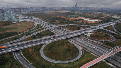 Aerial drone view of Chengdu cityscape with tall skyscrapers and elevated modern cloverleaf traffic junction. Dark grey sky in misty city, heavy traffic in developed metropolis Chinese city. Daytime.