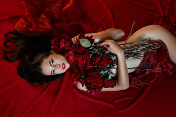 Beautiful sexy brunette with a bouquet of red roses lying on the floor, naked body parts, erotic...