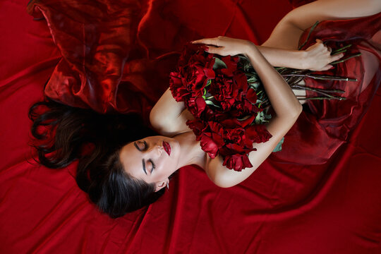 Beautiful sexy brunette with a bouquet of red roses lying on the floor, naked body parts, erotic portrait of a woman