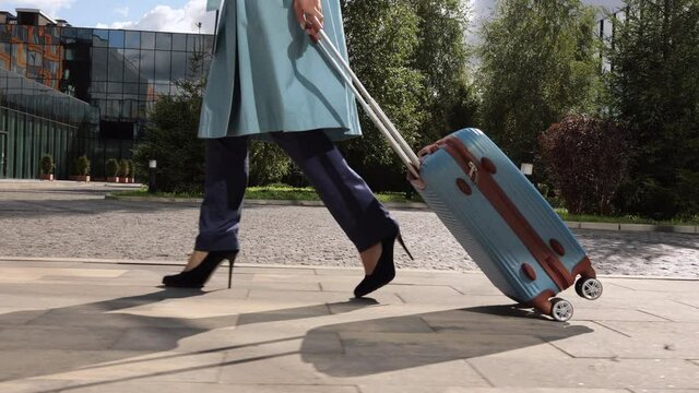 Closeup view of young woman walking through city with suitcase in hand and heading to airport spbi. Legs pic of beautiful businesswoman holds luggage and strolls confidently along glass building in