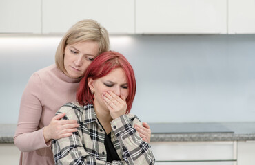 Woman hugs and calms her crying teen daughter at home. Teenagers problem concept. Empty space for text