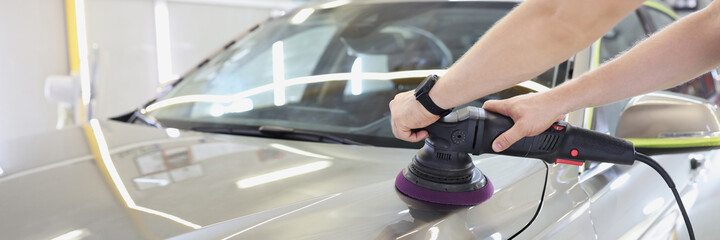 Worker with orbital polisher in auto repair shop closeup